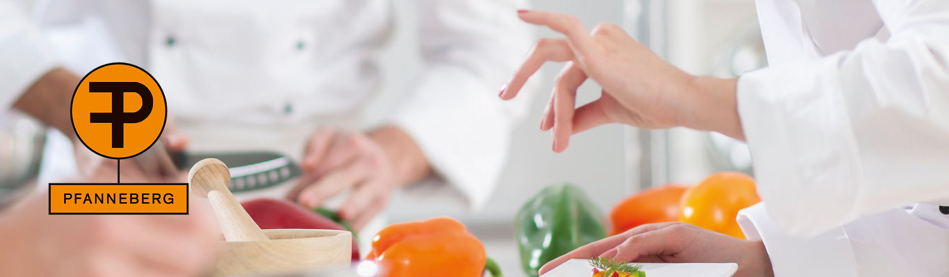 Ein Tisch in einer Küche, auf dem Paprika liegen, während das Küchenpersonal um den Tisch herum arbeitet und Zutaten vorbereitet. Hier finden Sie Fachbücher für die Berufliche Aus-, Fort- und Weiterbildung im Gastgewerbe.